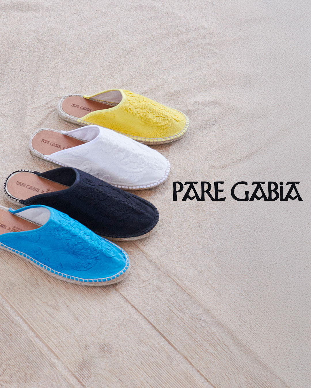 Four pairs of colorful open-back espadrilles neatly lined up on the sand